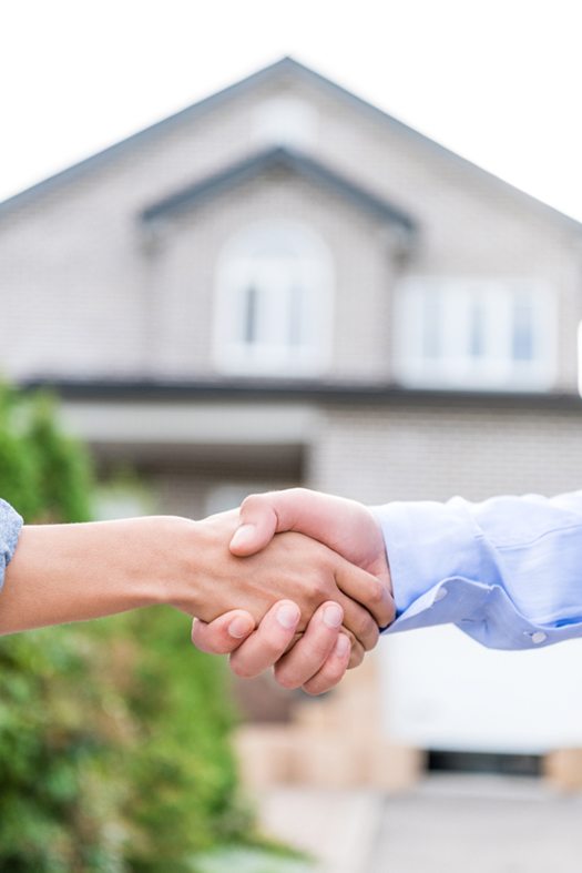 cropped shot of realtor and client shaking hands with blurred house on background