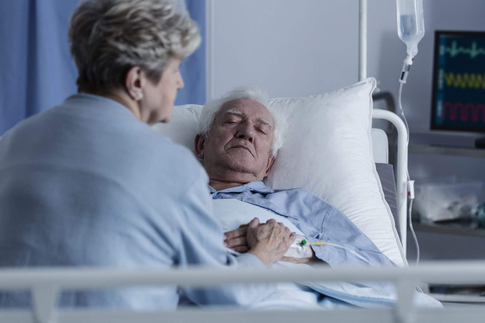 Blurred photo of a woman sitting by her husband's bed and praying with a rosary at the hospital
