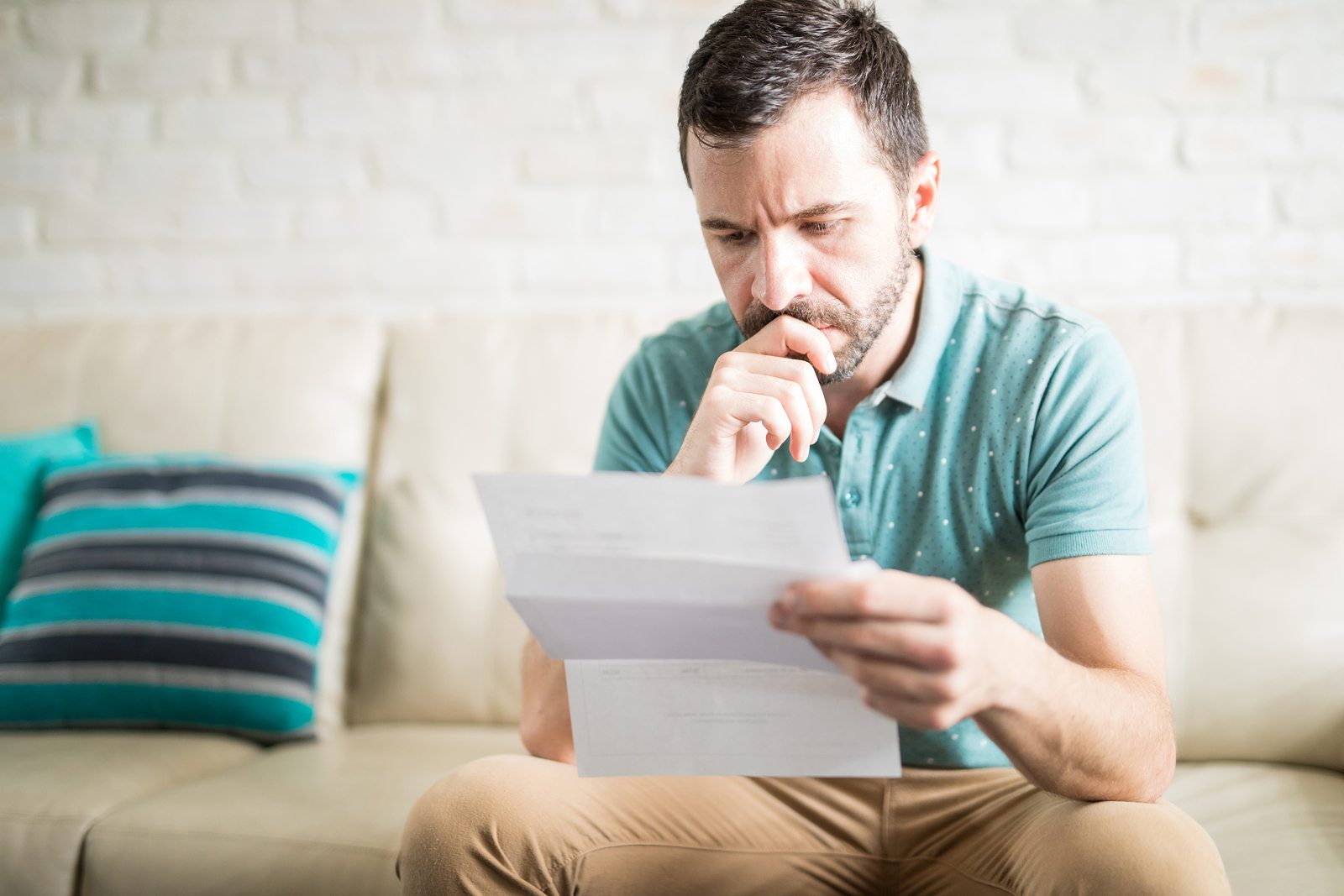 Handsome man sitting alone in the living room reading a letter and worried about some debt